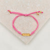 overhead photo of pink slip knot bracelet with gold medals and the word hope on white background