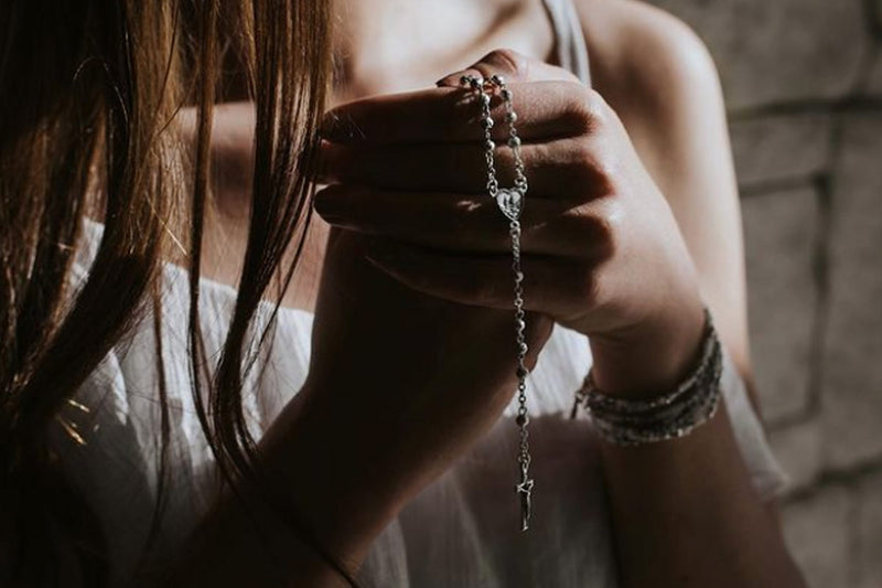 Young woman praying the rosary on a My Saint My Hero Beaded Medjugorje Rosary