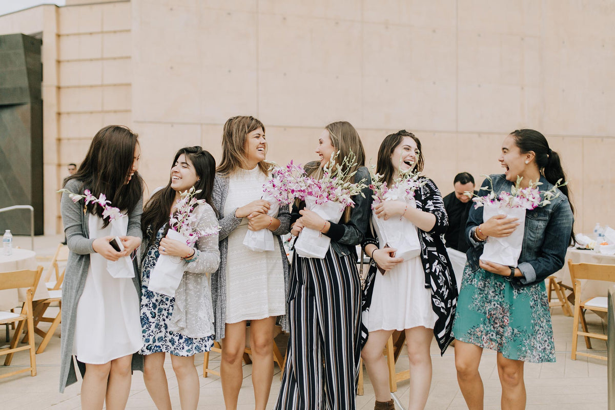 group of young women holding white paper bags of orchid flowers, laughing and chatting together