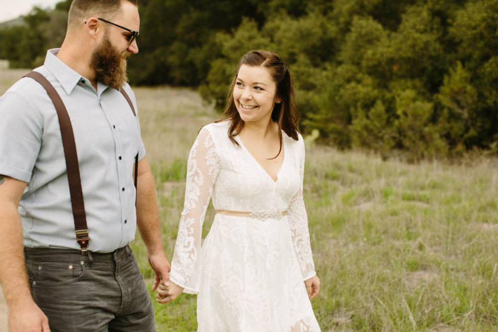 young man and woman holding hands, smiling at each other, walking in the grass