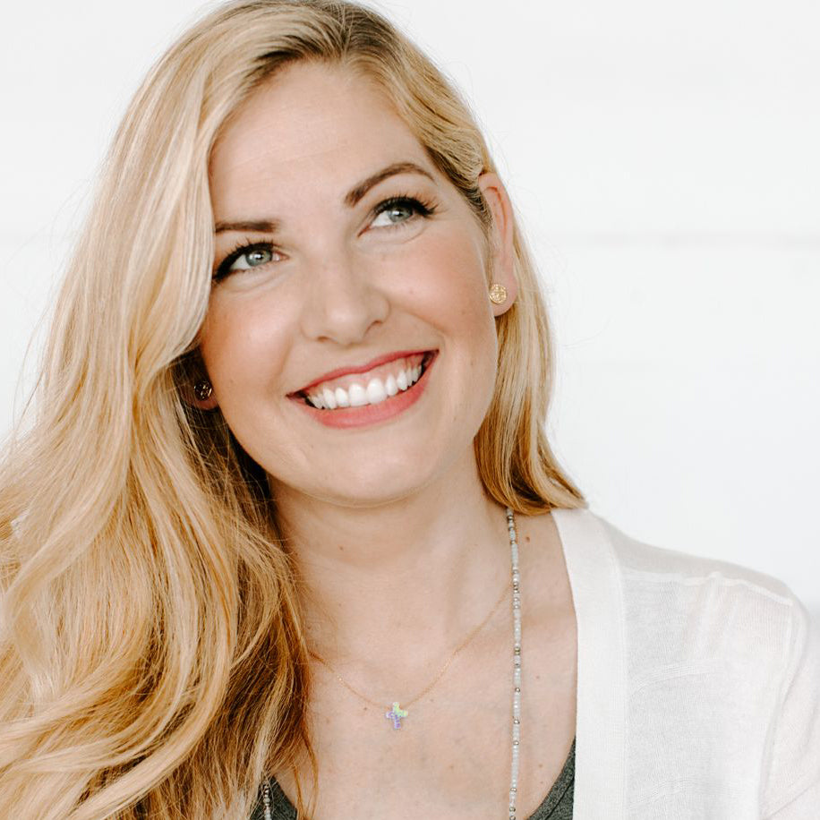 Smiling young woman with long blonde hair wearing My Saint My Hero necklaces