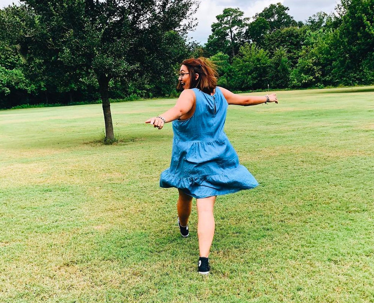 young woman running across a grassy field arms swinging wide