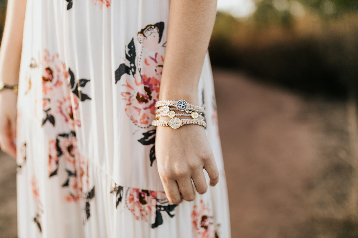 close up of woman in pink flowered white dress wearing a stock of My Saint My Hero Gratitude Blessing bracelets