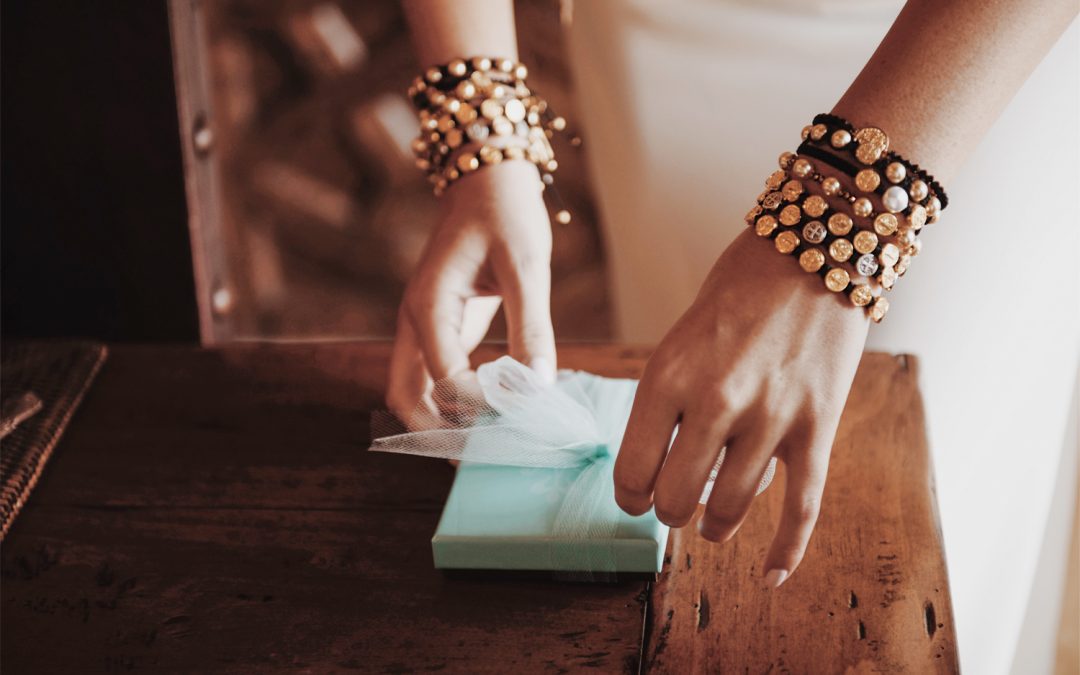 hands of woman wearing stacks of My Saint My Hero Blessing bracelets, tying a bow on a small gift package