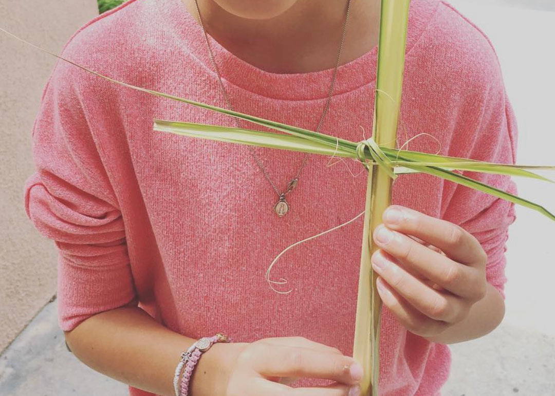 close up of child's hands holding a cross made of a palm leaf