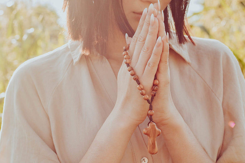 close up of woman in brown dress praying with a Wrap Rosary, wearing My Saint My Hero Blessing Bracelets 