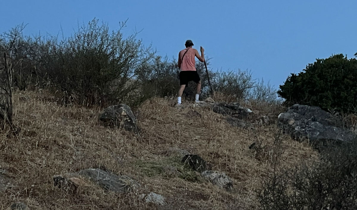 a man hiking up a hillside in magdala with blue sky wearing an orange shirt