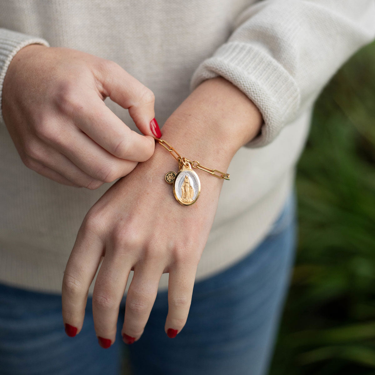 Hand holding a Malespine Our Lady of Lourdes tin, made in Lourdes since 1887, with a blessing bracelet on the wrist