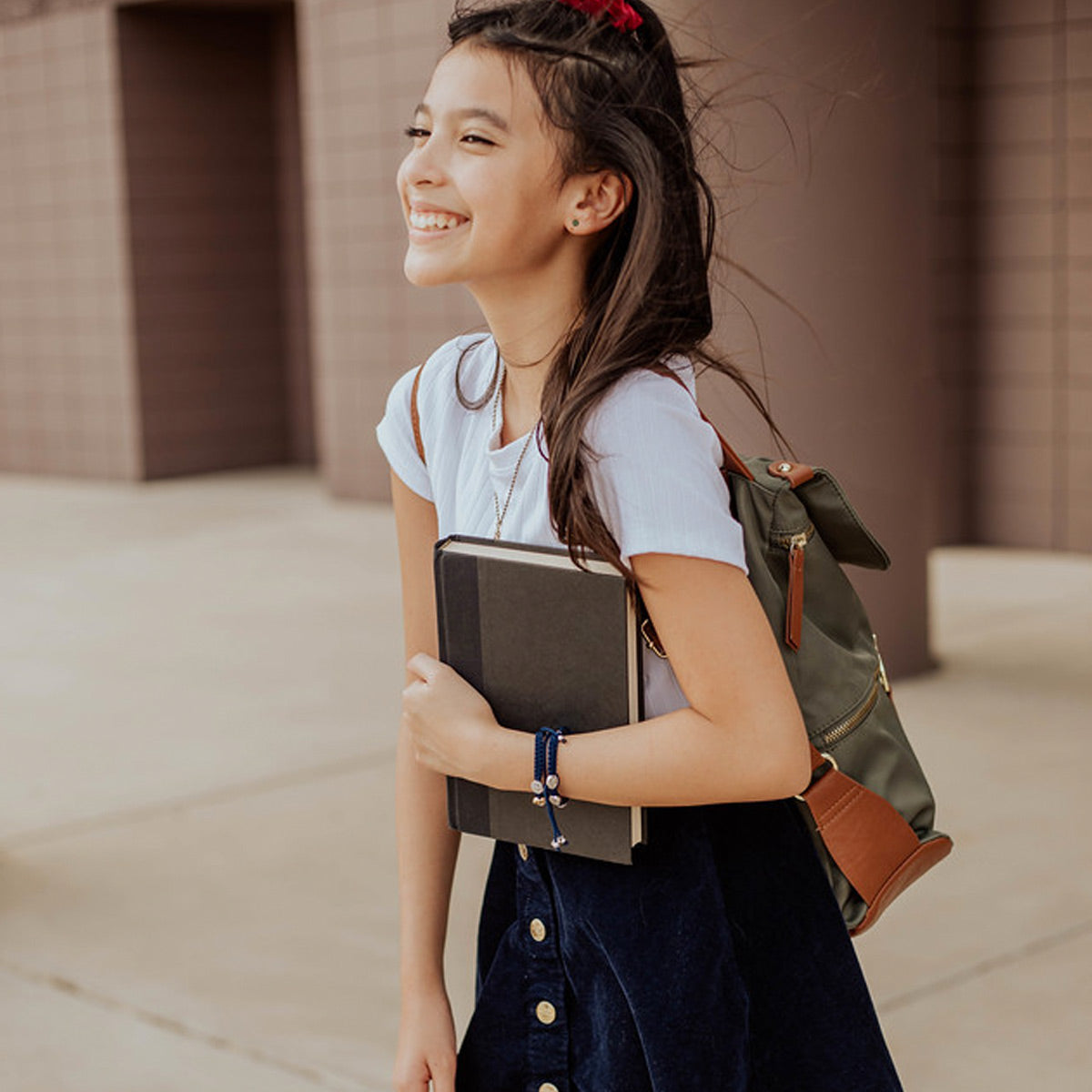 Back to School Collection image of girl with backpack, book, and stack of protection bracelets for kids