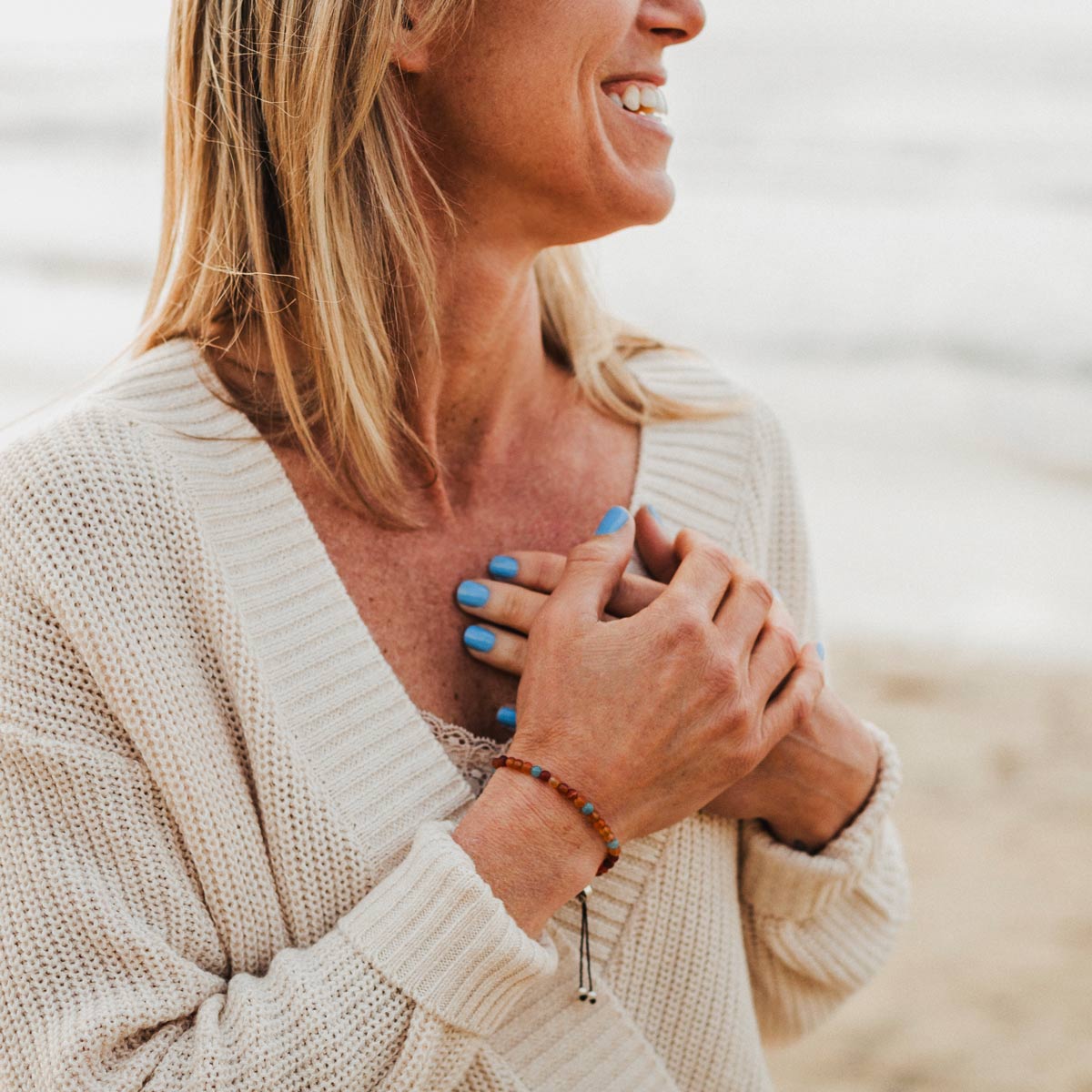 woman on beach wearing 7 stones of forgiveness bracelet holding her hands over her heart
