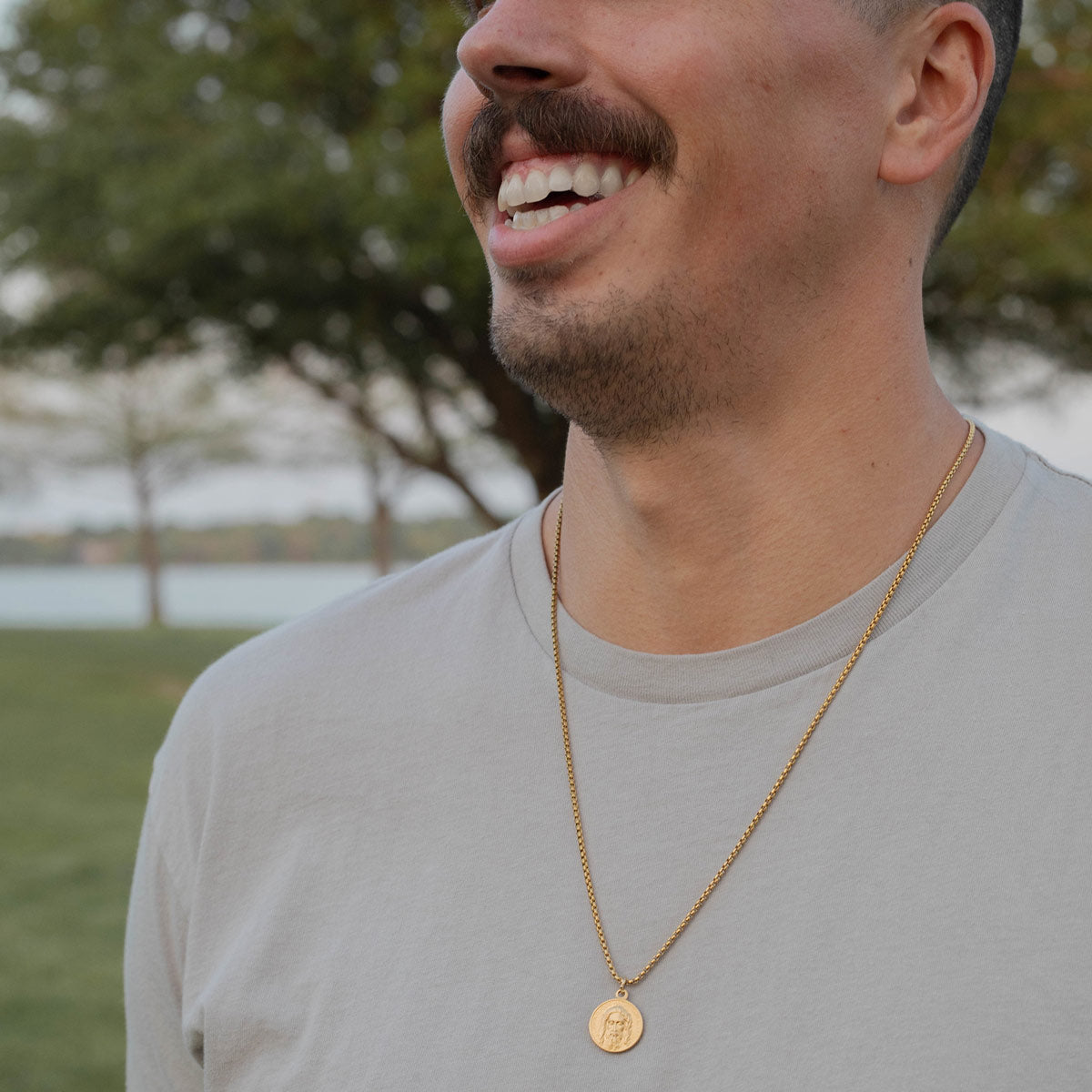 Black man wearing three woven saint medal bracelets in slate, cream and black, only his forearm and hand are visible, his hand is in his jeans pocket