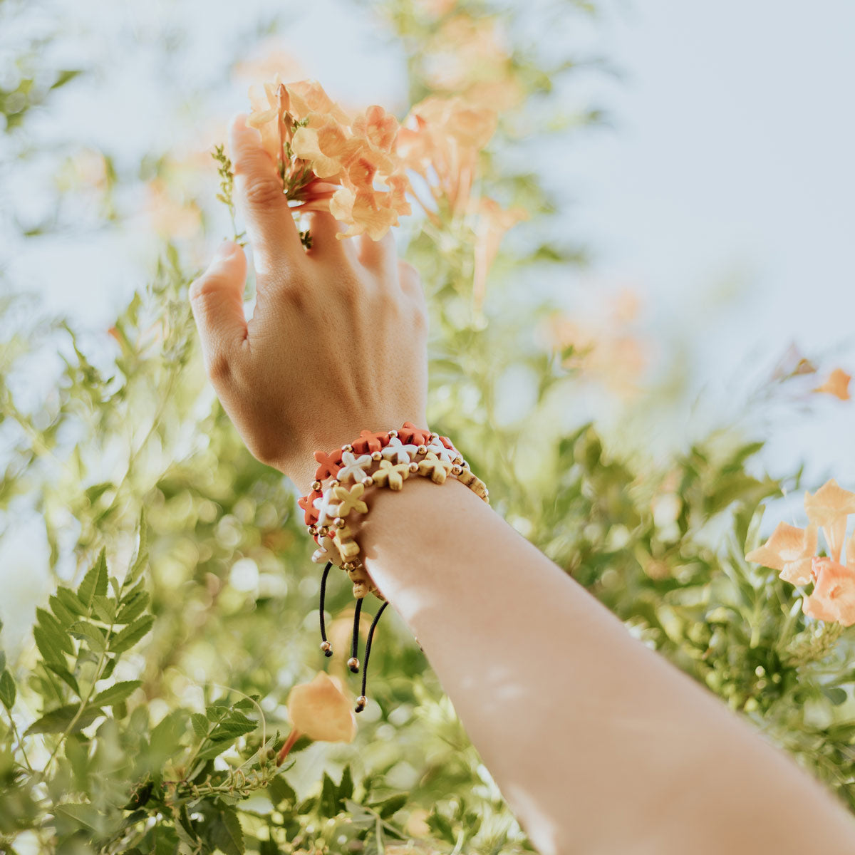 hand reaching toward flowering tree wearing spring bright cross bracelets in orange and yellow