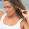 Woman at the beach wearing a Abide Pearl Cross Necklace