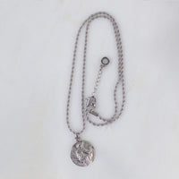 Silver round Archangel Gabriel guardian angel medallion pendant necklace displayed on its matching silver rope chain, showcasing the full length of the necklace and its adjustable lobster clasp closure, resting flat against a clean, white textured stone background.