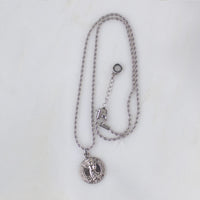 Silver round Archangel Michael guardian angel medallion pendant necklace displayed on its matching silver rope chain, showcasing the full length of the necklace and its adjustable lobster clasp closure, resting flat against a clean, white textured stone background.