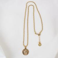 A full-length view of the gold Archangel Raphael Guardian Angel medallion necklace displayed against a smooth, white background. The round medal featuring the detailed engraving of the angel hangs from a long, delicate gold rope chain. The chain is arranged in a vertical loop, showing the clasp closure at the top right, complete with an adjustable extender chain and a small, round branded metal tag hanging at the end.