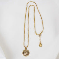 A full-length view of the gold Archangel Raphael Guardian Angel medallion necklace displayed against a smooth, white background. The intricate round medal hangs from a long, delicate gold rope chain that forms a vertical loop. On the right side, the chain displays its lobster clasp closure, an adjustable extender chain, and a small, round branded tag hanging at the very end.