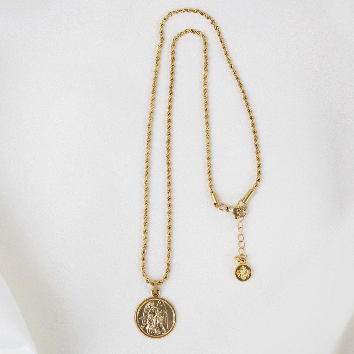 A full-length view of the gold Archangel Raphael Guardian Angel medallion necklace displayed against a smooth, white background. The intricate round medal hangs from a long, delicate gold rope chain that forms a vertical loop. On the right side, the chain displays its lobster clasp closure, an adjustable extender chain, and a small, round branded tag hanging at the very end.