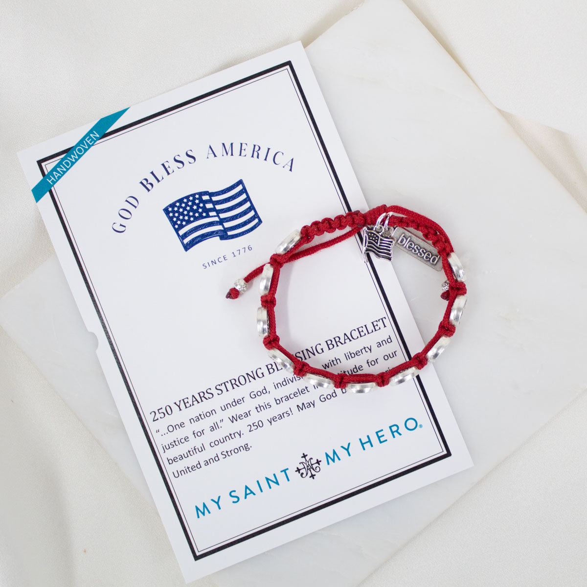 Red bracelet with 'Blessed' charm on a card with text and flag design, on a white surface.