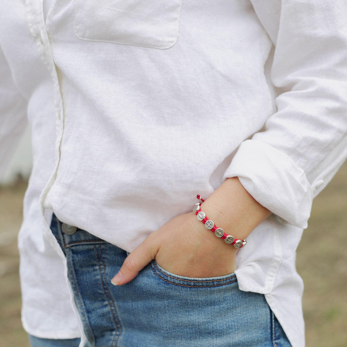 Person wearing a white jacket and blue jeans with a red bracelet on a blurred background