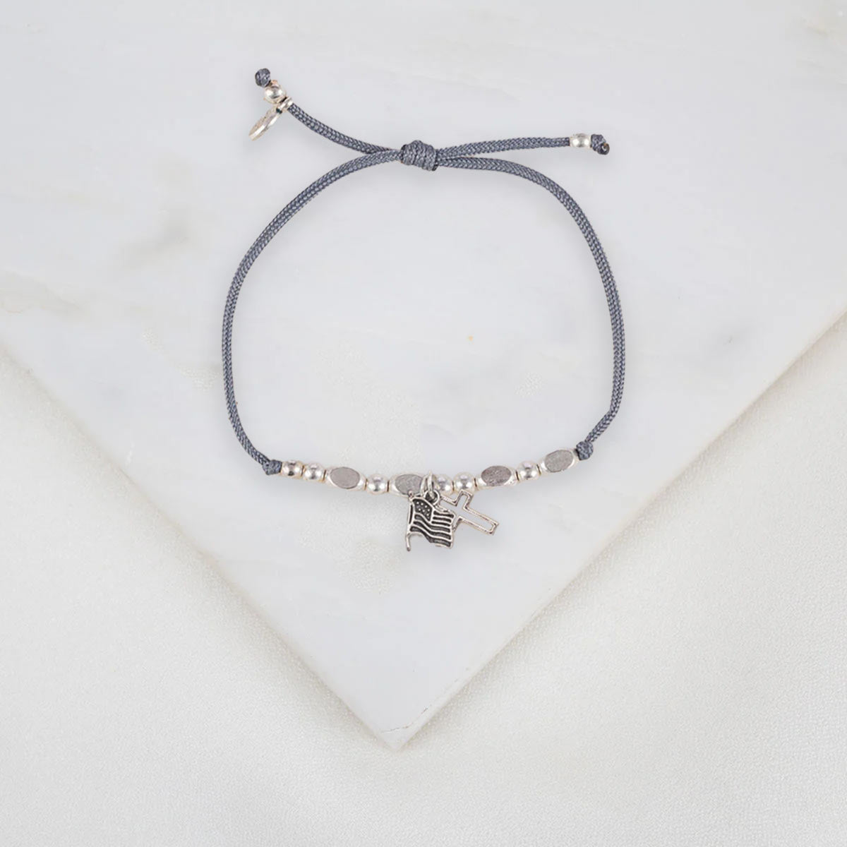 Gray handmade slipknot bracelet with silver beads and with a cross and an American flapg charm on a light gray background