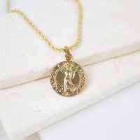  Gold round Archangel Michael guardian angel medallion pendant on a gold rope chain, resting on a white textured stone surface. The medal features a detailed engraving of St. Michael defeating a dragon with the inscription "S. MICHEL ARCHANGE".