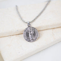 Silver round Archangel Michael guardian angel medallion pendant on a silver rope chain, resting on a white textured stone surface. The medal features a detailed engraving of St. Michael defeating a dragon with the inscription "S. MICHEL ARCHANGE".