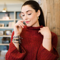 woman in red sweater wearing a gold breathe chain bracelet and woven my saint my hero bracelets