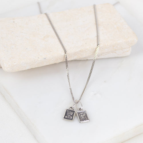 Silver necklace with two pendant charms on a white surface
