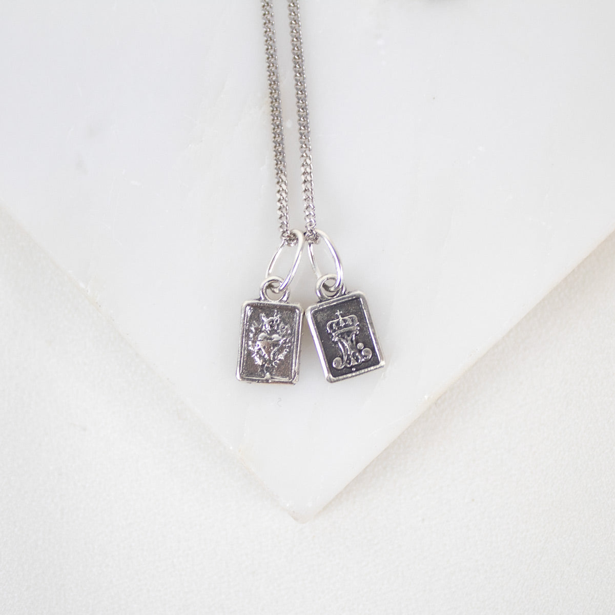 Silver necklace with two book-shaped sterling silver sacred heart scapular pendants on a white background