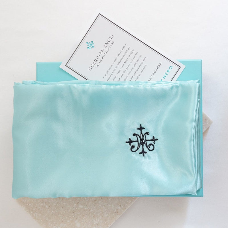 A blue satin pillowcase with embroidered detailing, presented in a box with a card.