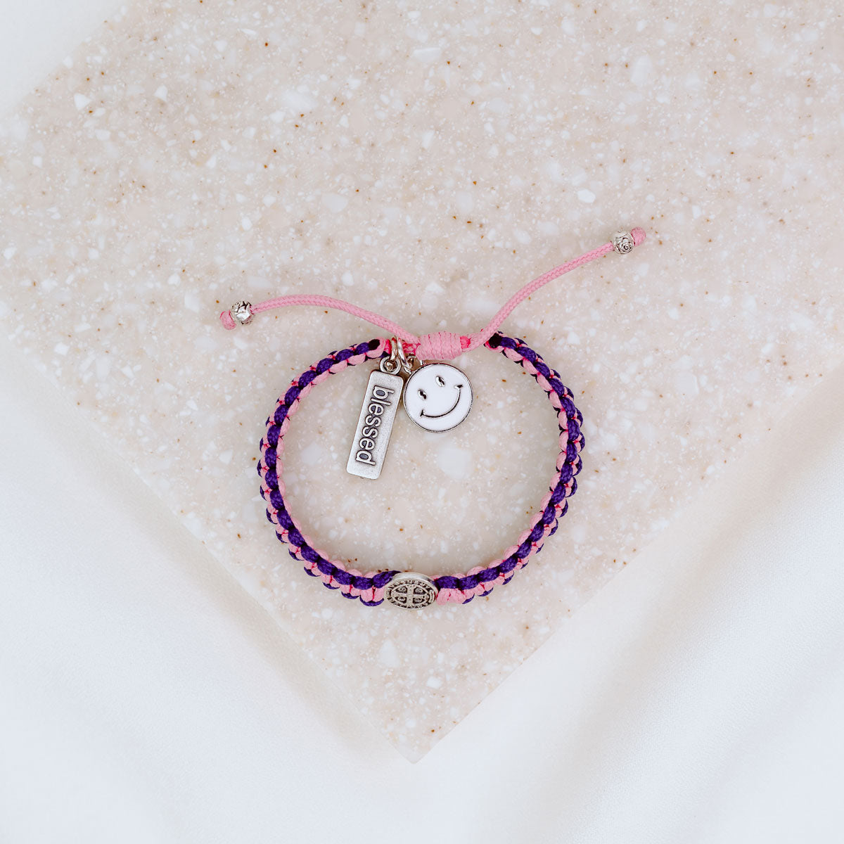 Kids Benedictine pink purple thread handwoven blessing bracelet with silver tone blessed charm and white enamel happy face
