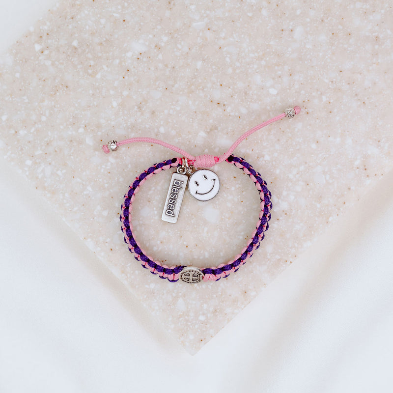 Kids Benedictine pink purple thread handwoven blessing bracelet with silver tone blessed charm and white enamel happy face
