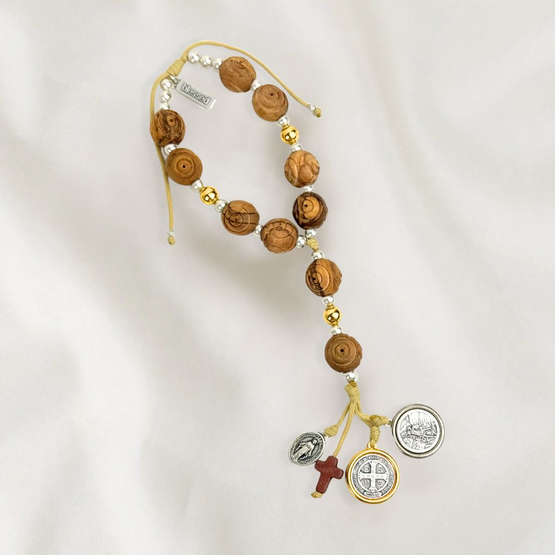 A door hanger made of hand-carved olive wood, featuring a two-tone Benedictine medal, a howlite cross, and silver-tone Miraculous Mary and Archangel Michael medals.