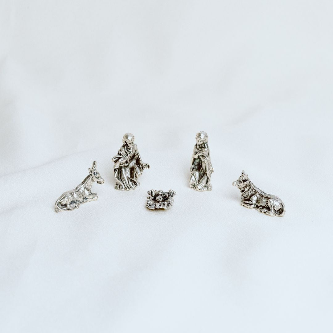 A silver-tone nativity set with figures of the Virgin Mary, Joseph, and baby Jesus, along with a dog and a wolf.