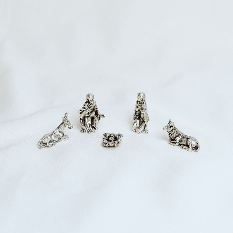 A silver-tone nativity set with figures of the Virgin Mary, Joseph, and baby Jesus, along with a dog and a wolf.