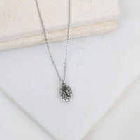 Silver necklace with the back of the Miraculous medal charm pendant on a white surface