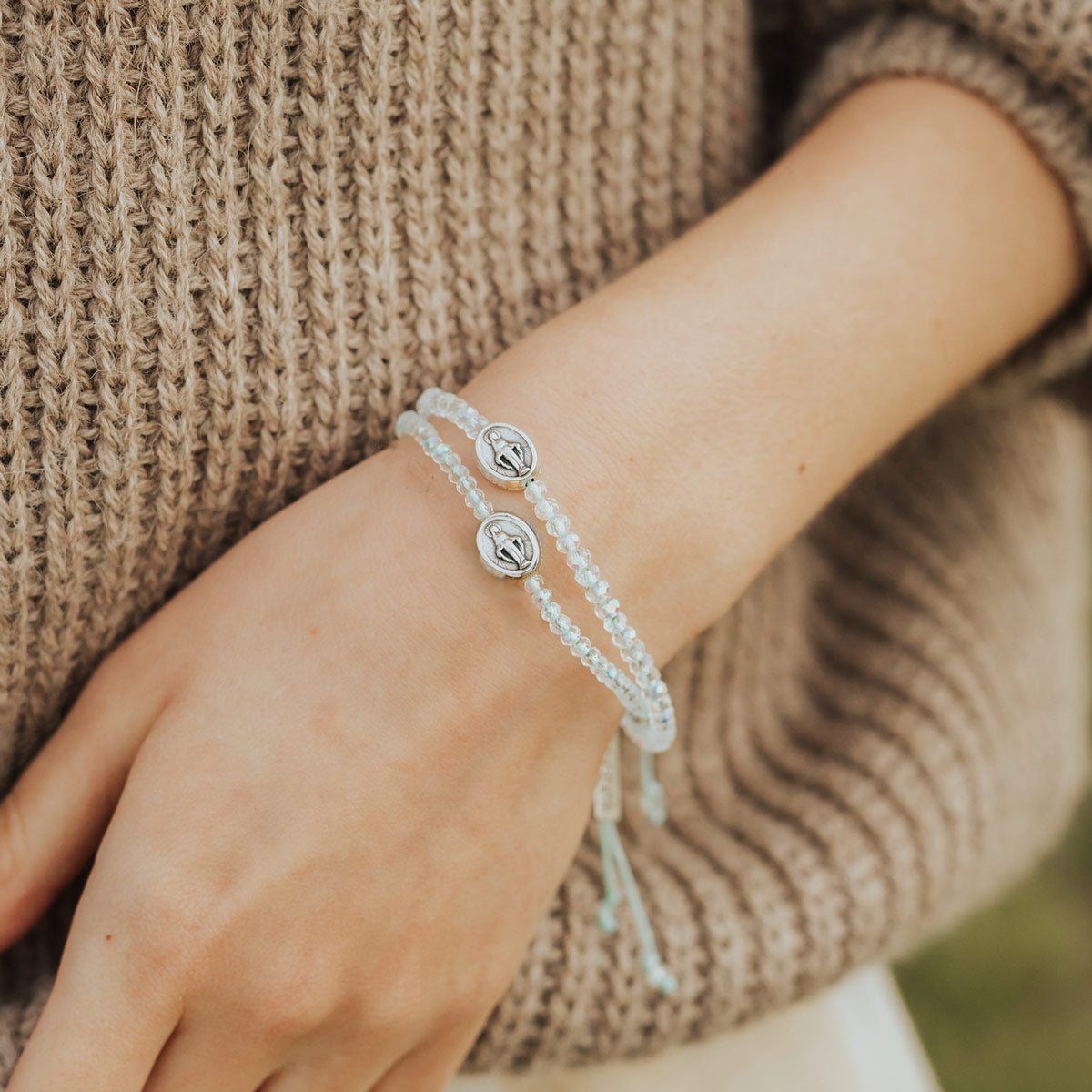 Close-up of a wrist wearing the handwoven crystal Quinceañera Promise Bracelet with its silver-tone Miraculous Mary Medal.