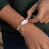 Person wearing a silver bracelet with a detailed design on their wrist.