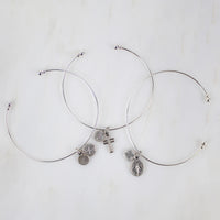 Flatlay of three silver whisper bangles with a cross, st. benedict, and miraculous medal