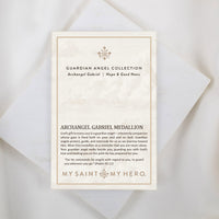 The front of a My Saint My Hero informational product card for the Archangel Gabriel Guardian Angel Necklace, resting on a white textured stone surface. The cream-colored card features the heading "GUARDIAN ANGEL COLLECTION" and "Archangel Gabriel | Hope & Good News" with a small decorative cross symbol at the top. The lower section is titled "ARCHANGEL GABRIEL MEDALLION" and features an inspirational paragraph about guardian angels alongside a quote from Psalm 91:11. The "MY SAINT MY HERO" brand logo is di