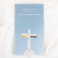 The back of the Booklet with  'MY SAINT MY HERO.' with a white cross illustration on the cover, photographed flat on a white fabric background.