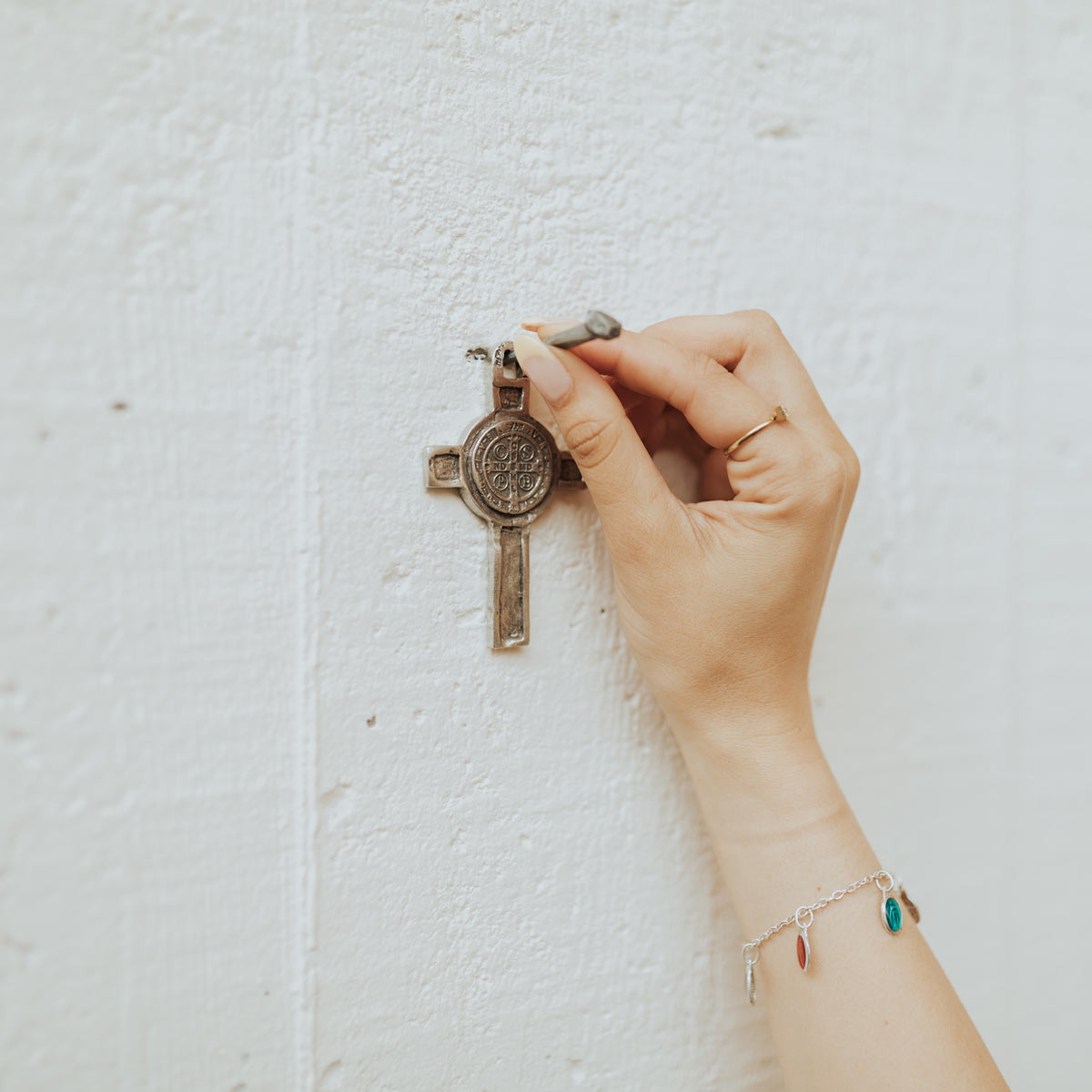 Hand holding a small cross against a textured white background