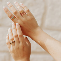 Two hands with gold rings on a neutral background