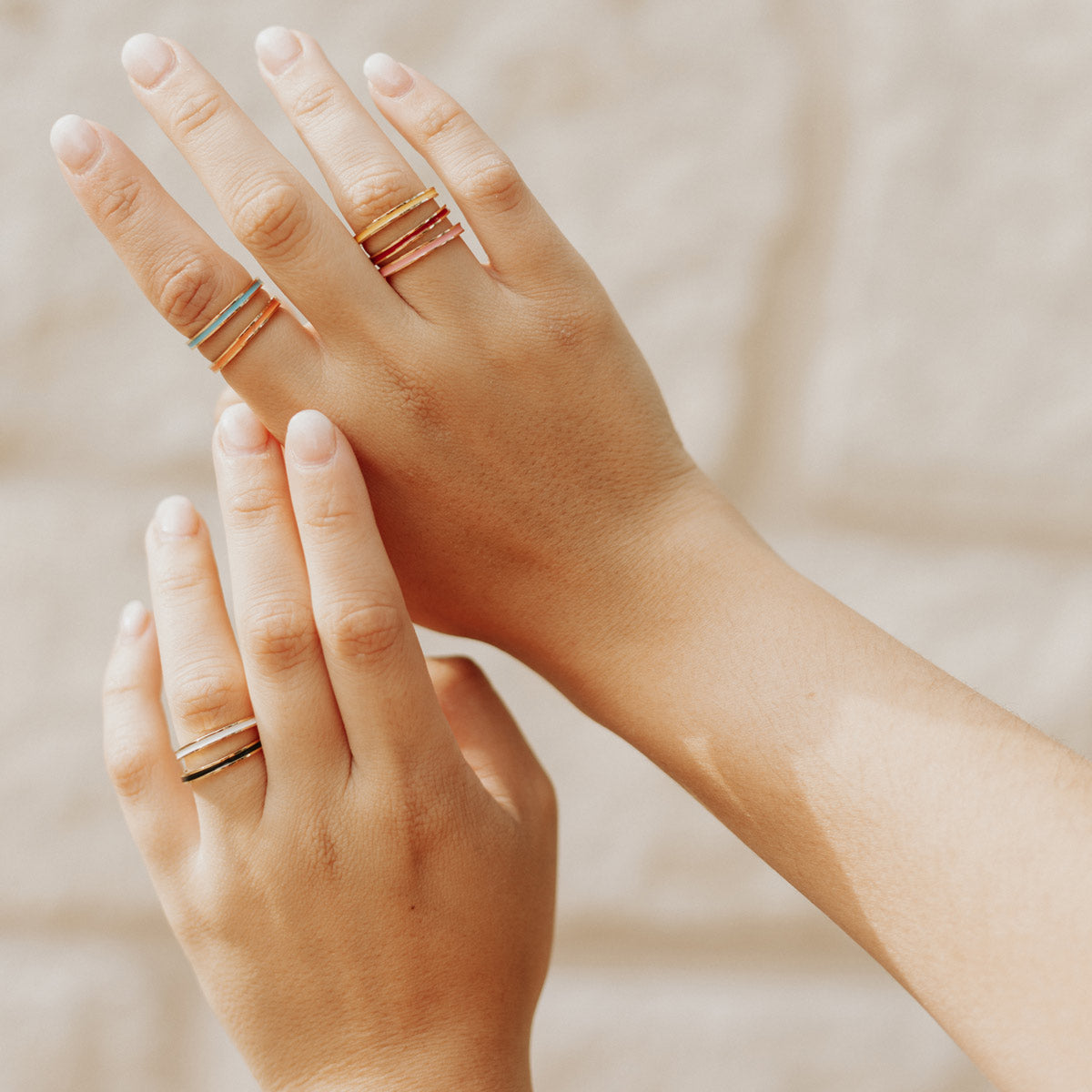Two hands with gold rings on a neutral background