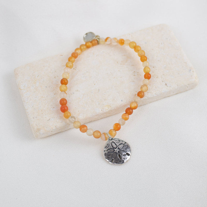 Beaded bracelet with a silver charm on a white stone surface