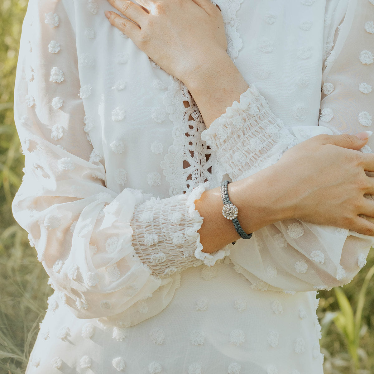 A close-up of a person wearing a Brilliance Blessing Bracelet paired with a white embroidered blouse in an outdoor setting.