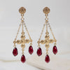 Gold earrings with red teardrop beads on a light background