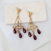 Gold earrings with red crystals on a white marble surface