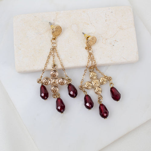 Gold earrings with red crystals on a white marble surface